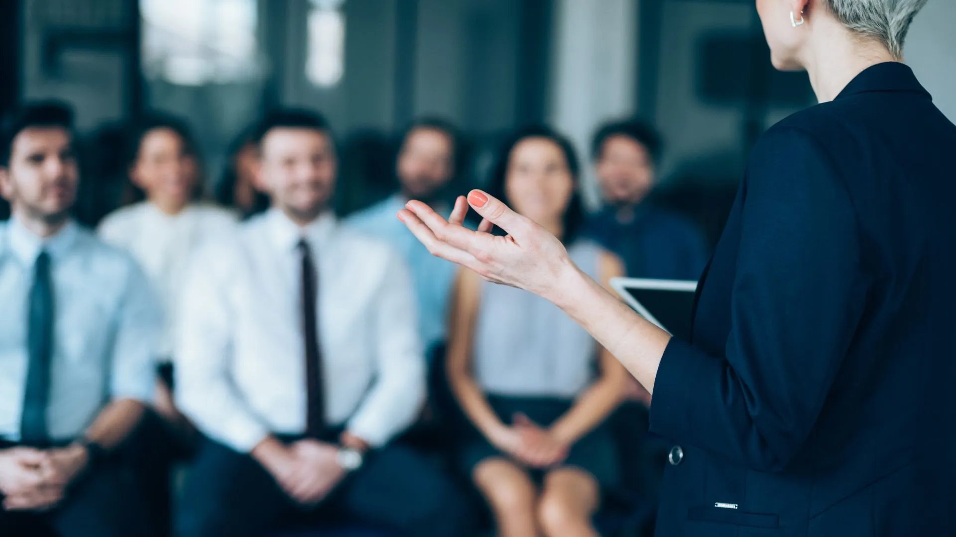A woman discussing why phishing training is important is being listened to by a crowd of business people