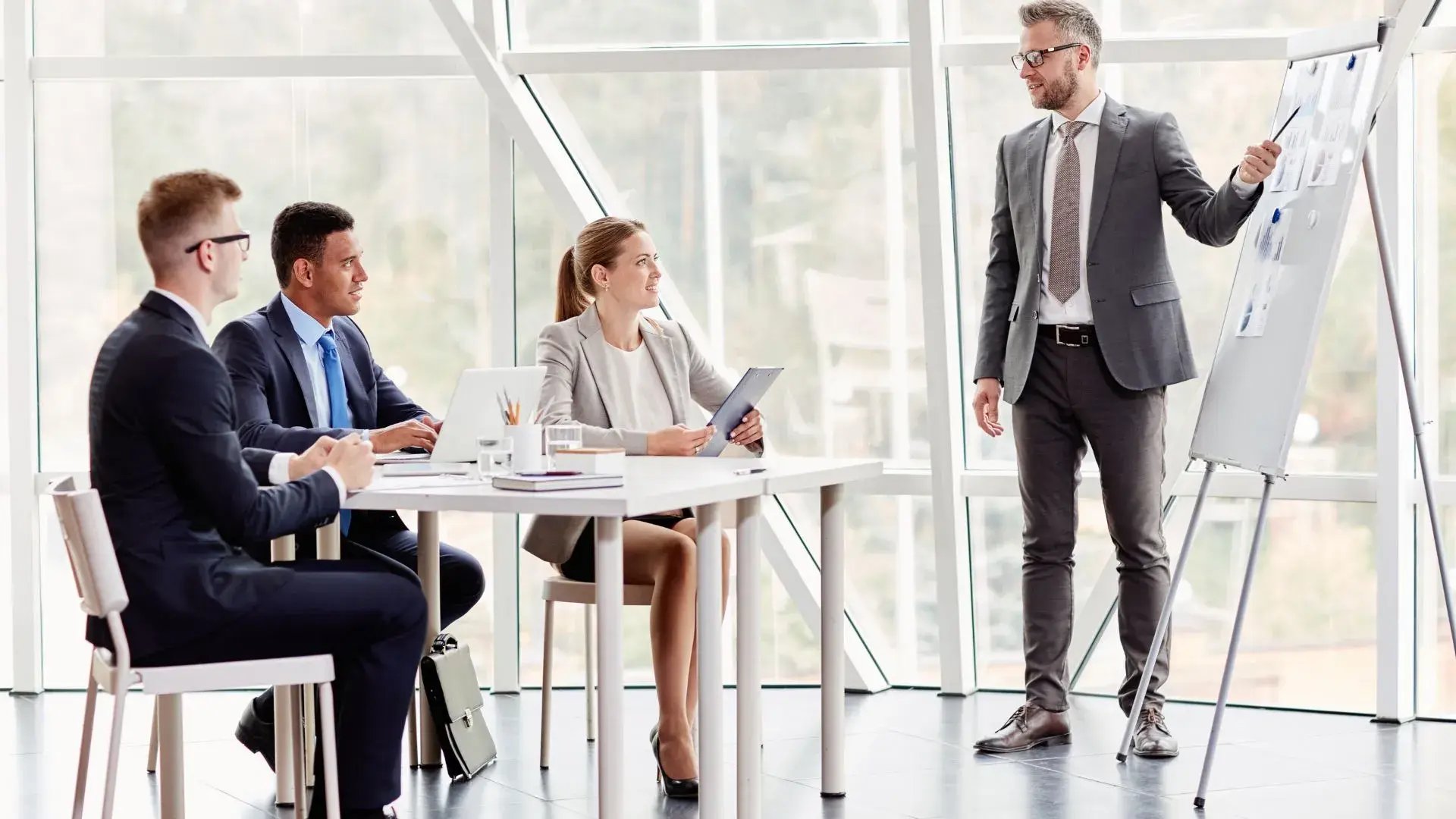 Four people dressed in corporate wear are having a training session. One of the four is presenting something on the whiteboard while the other three are listening to his discussion.&nbsp;