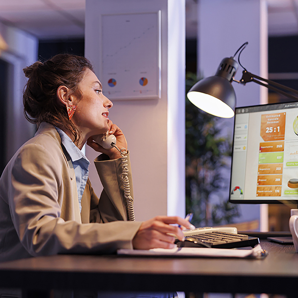 Woman using phone and office computer to manage her online store