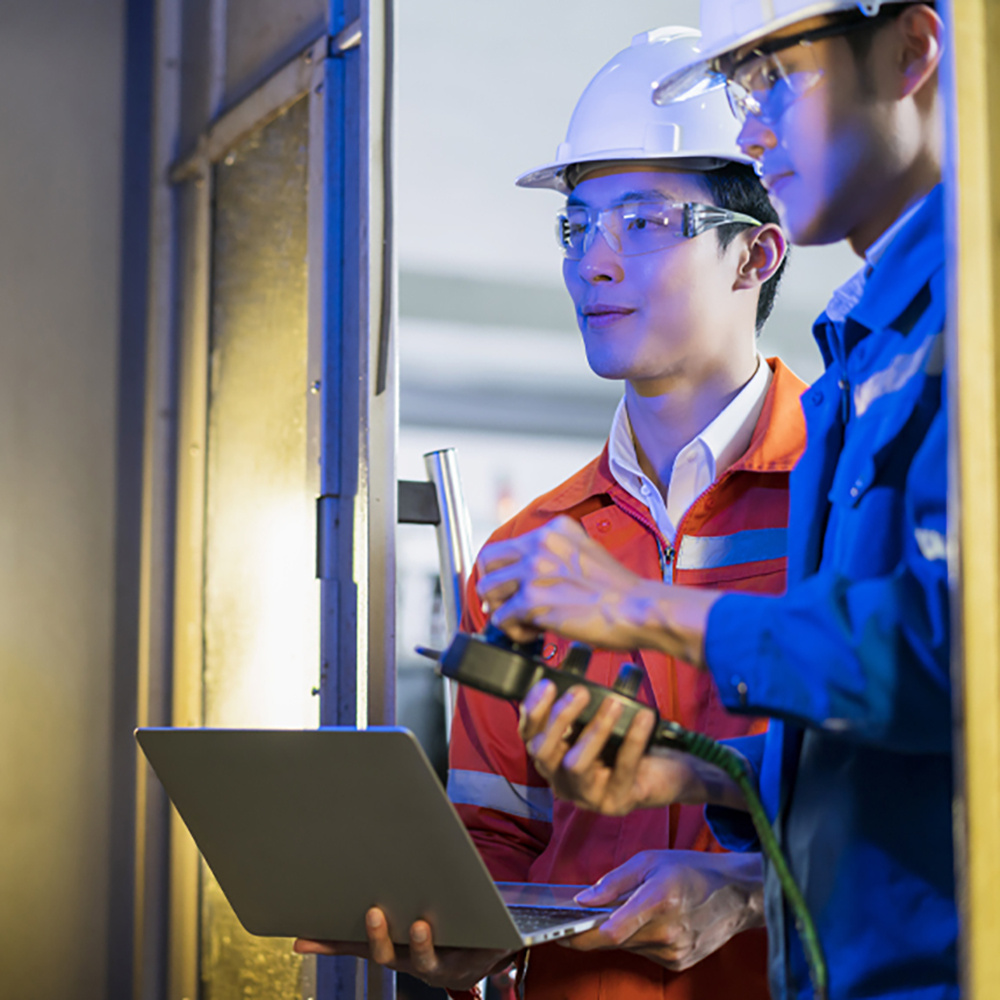 Two technicians with safety gear using laptop in manufacturing plant